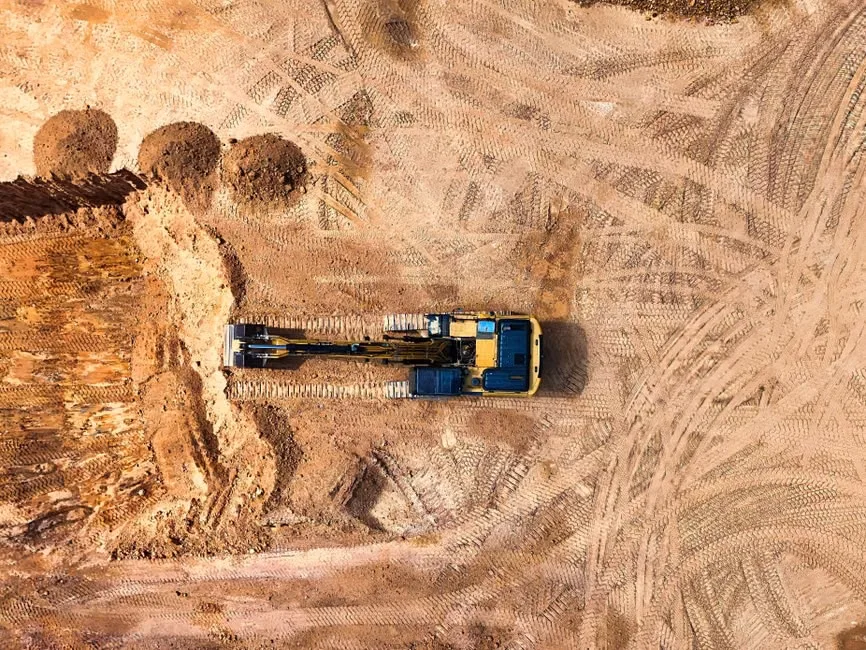Aerial view of an excavator clearing and grading a sandy Florida construction site